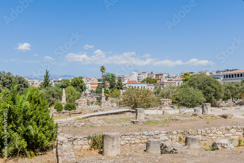 Ancient ruins in a field with a modern city and clear blue sky in the background, in Athens, Greece
