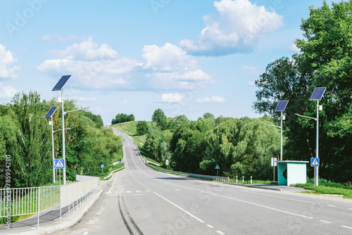 Lamp post with solar panel system on road with blue sky and trees. Autonomous street lighting using solar panels. Street lamp, on batteries from the sun. Alternative renewable energy systems