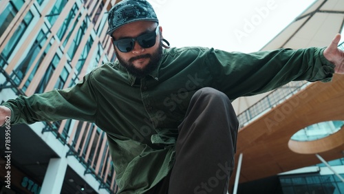 Low angle view of hipster pose in hip hop style surrounded by mall view. Portrait of sporty asian hip hop choreographer dancing break dance while looking at camera. Outdoor sport 2024. Endeavor.