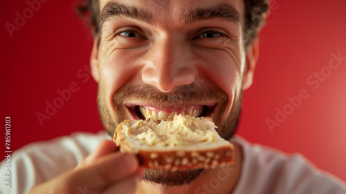 A man is eating a sandwich with a smile on his face. The sandwich is made of bread and has a spread on it. A close frontal view of a Swiss man savoring a bite of bread with creamy hummus