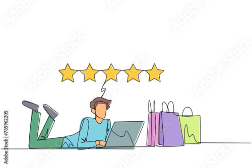 Continuous one line drawing young smiling man on stomach while typing on laptop. Next to the laptop is a shopping bag. Give the best review with pleasure. Single line draw design vector illustration
