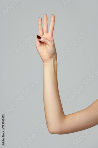 Female hand showing three fingers up on gray background