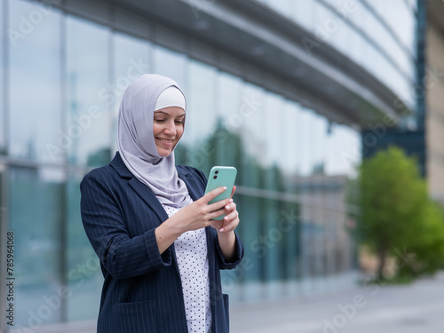 Business woman in hijab and suit using smartphone outdoors. 