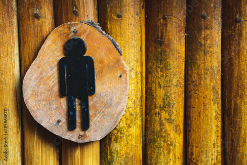 Sign symbol MAN on the door of a public toilet with a background of arranged wood and bamboo. Restroom sign on a toilet door. Man WC signs for restroom. 