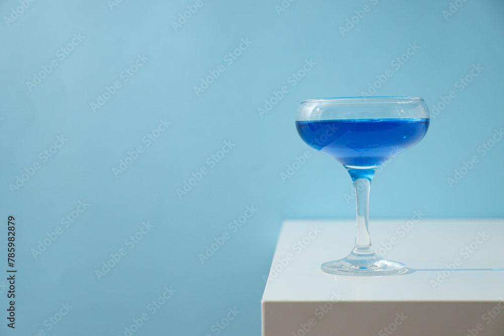 Blue drink in cocktail glass on blue background, space for text Blue drink in cocktail glass on blue background, space for text