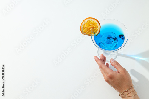 Blue cocktail with orange slice in glass and hand on white background  space for text