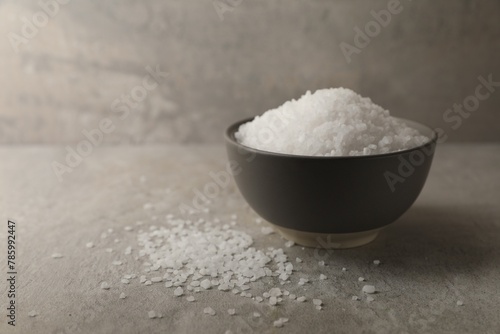 Natural salt in bowl on grey textured table, space for text