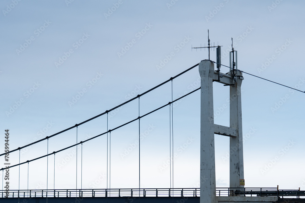 Fototapeta premium Closeup view of a suspension bridge pillar with cable line set for transportation cross in a calm blue sky during daylight