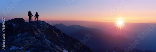  A Couple climber on a mountain peak at dawn that paints the sky with spectacular colors and standing on top of mountain with backpacks on morning sky is a bright orange and the sun peeking over the   photo
