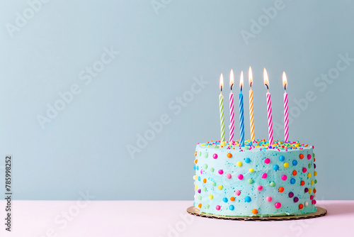 Birthday cake with candles stands on table on blue background with copy space.