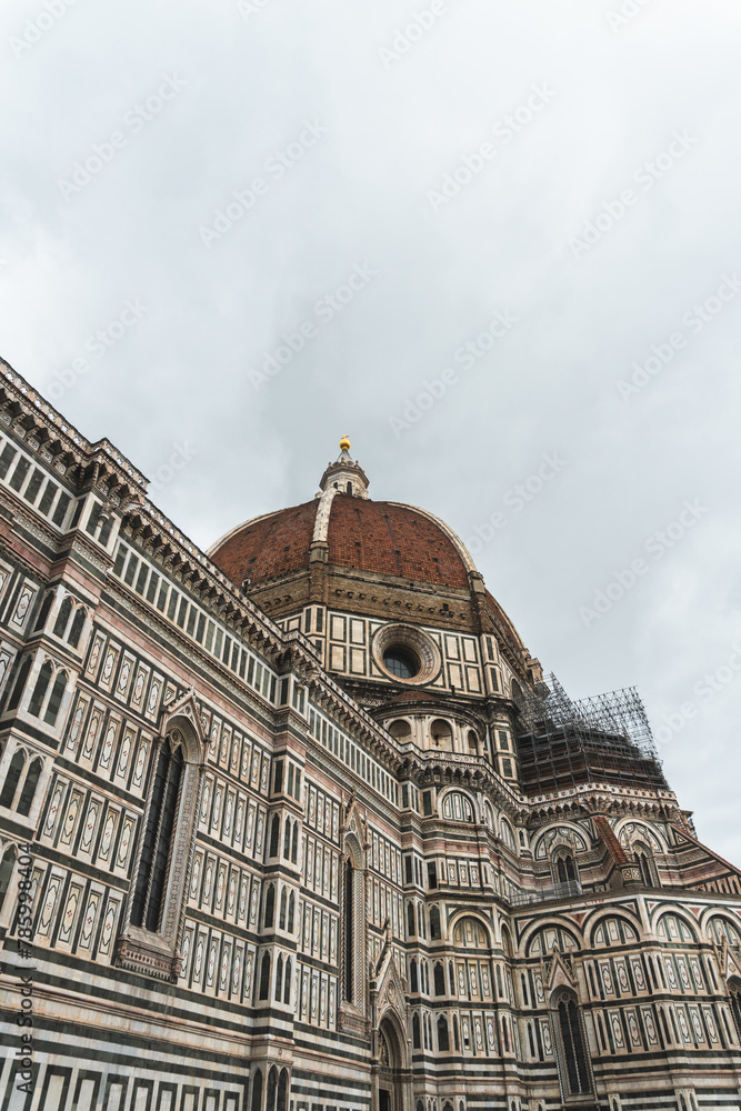 Iconic Duomo di Firenze facade with its towering dome under renovation. Overcast sky sets a dramatic backdrop to the timeless beauty of Florence.