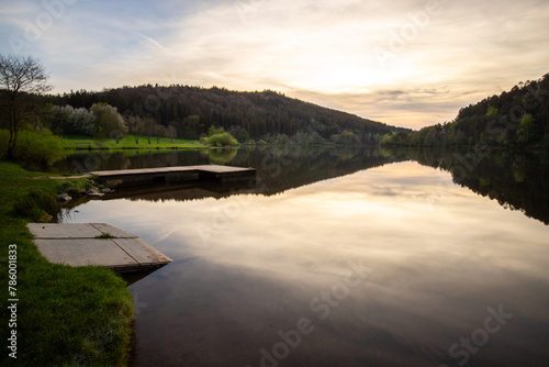 A lake in a landscape shot. A sunset and the natural surroundings are reflected in the water of the reservoir. Marbachstausee, Odenwald, Hesse photo