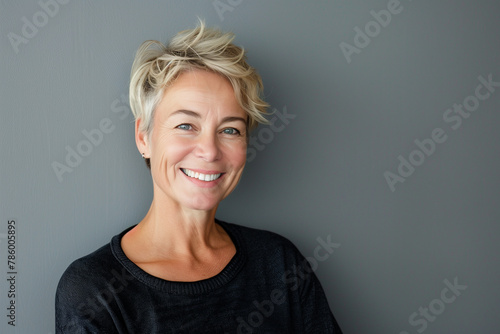 Portrait of a middle-aged woman with short blonde hair smiling at the camera on a gray background, studio shot photo