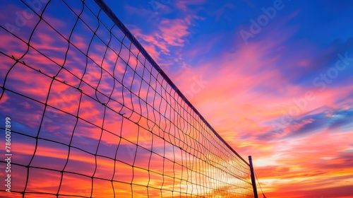 A close-up of a volleyball net against a vibrant sunset sky, with players silhouetted in the background. 