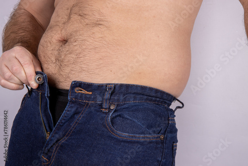 A middle aged slightly over weight man, trying to put on a pair of jeans but they wont fasten due to the man putting on weight and needed to go on a diet, dieting needed concept.