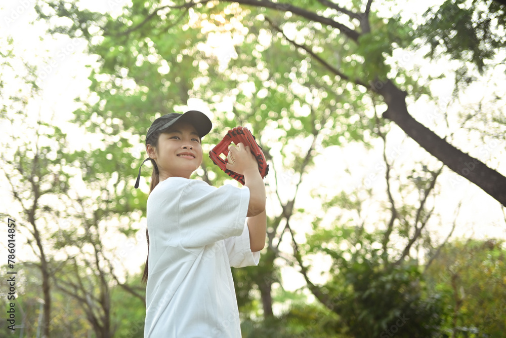 Joyful asian girl in leather glove playing baseball on green grassy lawn during summer day Joyful asian girl in leather glove playing baseball on green grassy lawn during summer day