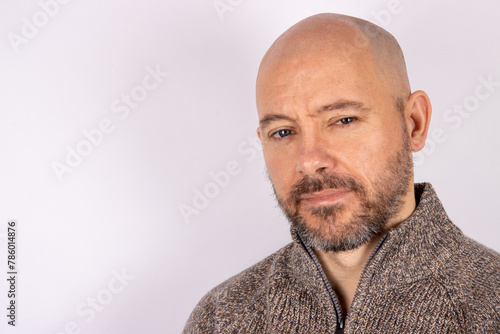 A middle aged bald shaven headed man with a beard wearing a jumper on white background