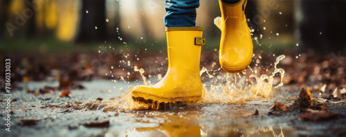 Happy kid splashing in puddles with yellow rubber boots. © Michal
