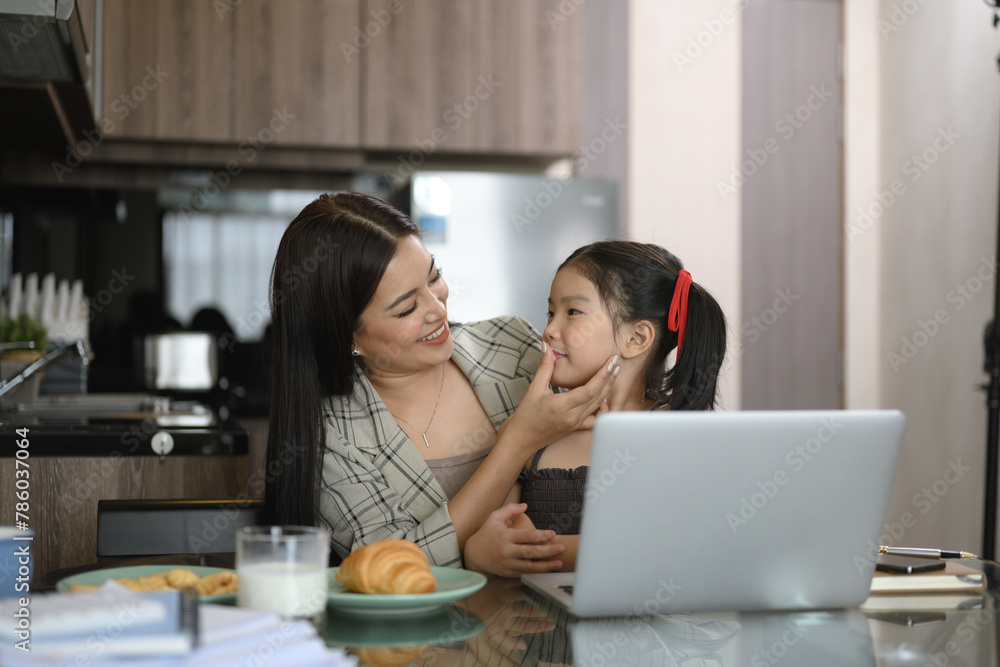 Beautiful working mom using a laptop and spending time with her little daughter at home