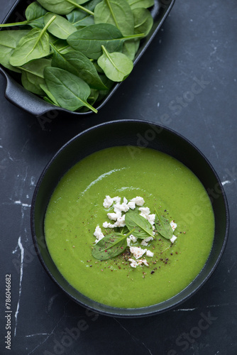 Bowl of freshly made spinach cream-soup on a black marble background, vertical shot, high angle view