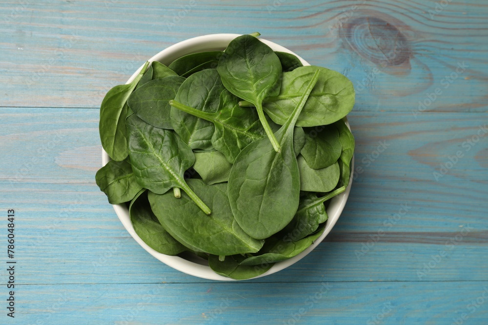 Fresh spinach leaves in bowl on light blue wooden table, top view Fresh spinach leaves in bowl on light blue wooden table, top view
