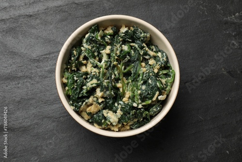 Tasty spinach dip with egg in bowl on black table  top view