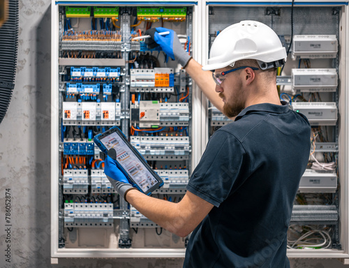 Φωτογραφία Electrical technician working in a switchboard with fuses, uses a tablet