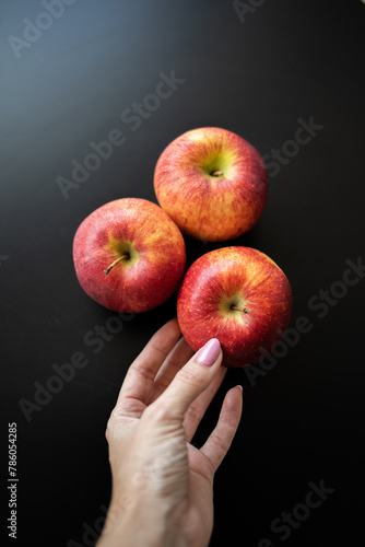 A woman places three red apples on a black background