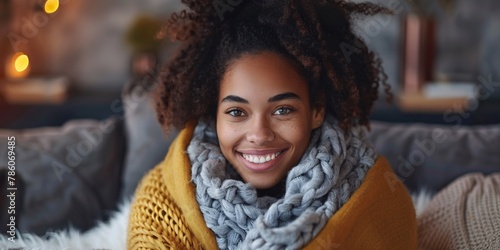 Gorgeous ebony lady lounging on sofa, giggling while covered in cozy throw. Joyful Afro-American female enjoying carefree moment at home, embracing herself with snug wrap during chilly season. photo