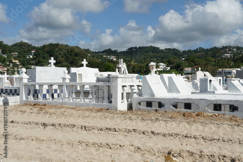 White tombstones and graves in a cemetery near the beach in Castries, Saint Lucia, one of the Caribbean islands with mountains in background.  