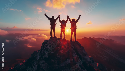 Three hikers triumphantly raise their arms atop mountain peak as sun sets behind them, casting warm glow over the majestic landscape. Active people, beauty in Nature and friendship concept. photo