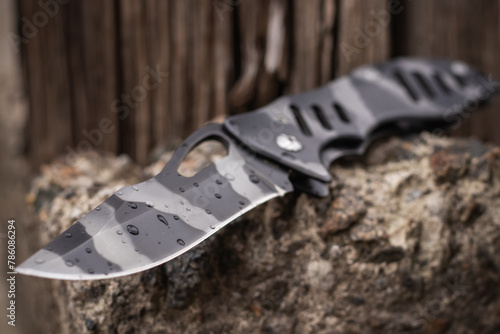 Tactical folding knife with water drops for survival on stone background