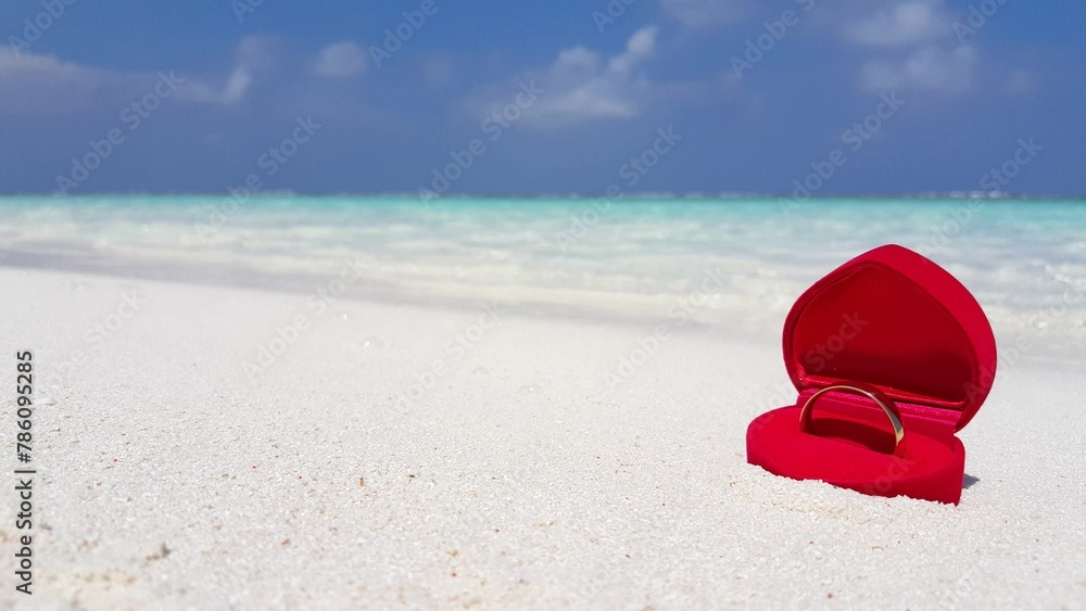 Closeup of a wedding ring in the red heart-shaped box on the sand of a tropical beach Closeup of a wedding ring in the red heart-shaped box on the sand of a tropical beach