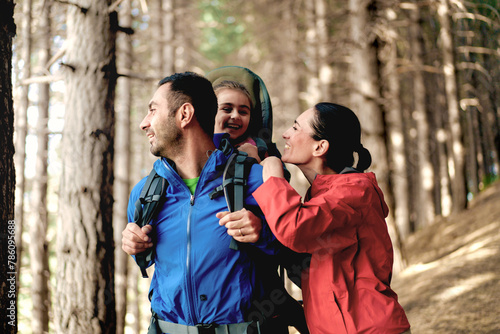 Family enjoys hike through the forest - young daughter happily seated in a child carrier backpack - joy of discovery and beauty of nature together.