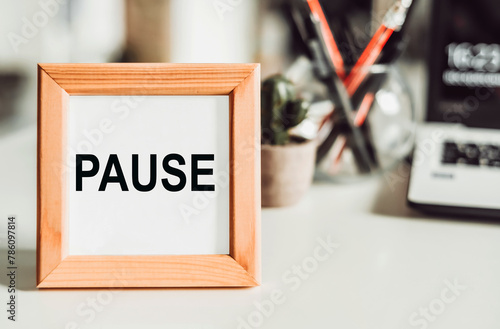 Wooden frame with the words pause and reflect. The word pause and reflect with time in the background of the office.