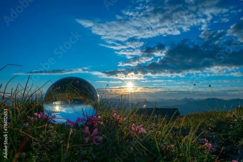 Crystal ball laying on the field with the bright sunset and the blue sky reflected in it