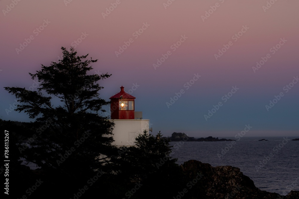 Red lighthouse behind trees at sunset in Vancouver Island