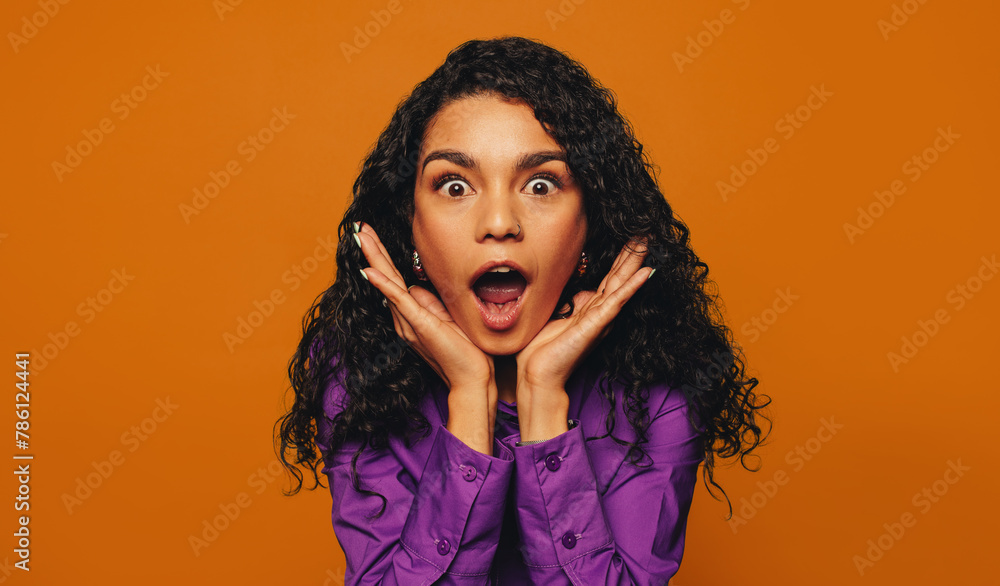 Surprised woman with curly hair on vibrant orange background Surprised woman with curly hair on vibrant orange background