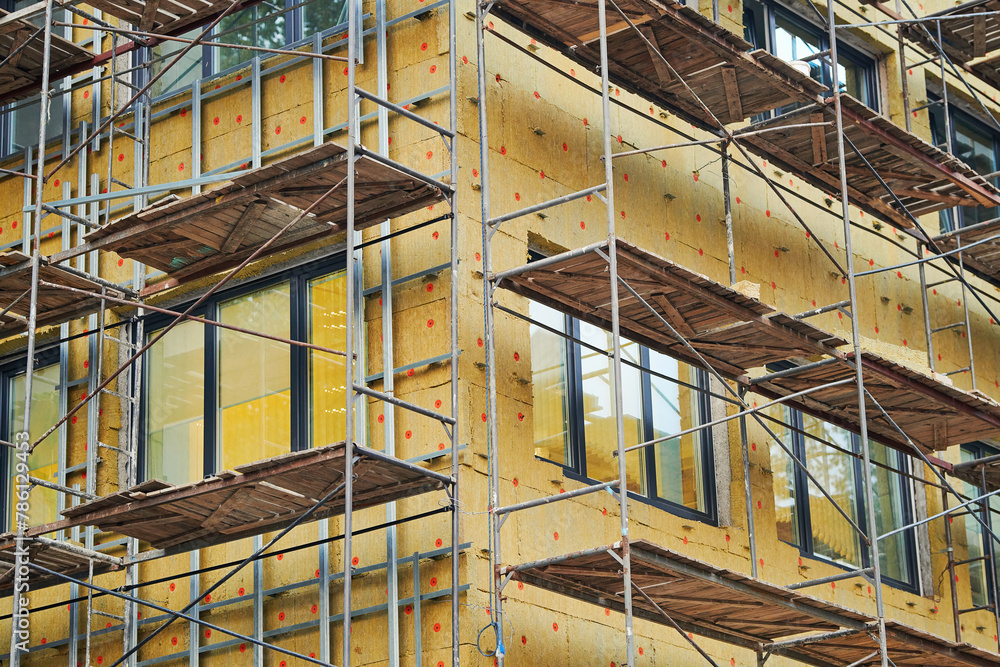 Wall insulation of building wall with mineral wool. Scaffolding, aerial work, insulation of building facade, heat improvement and facing work. Installing thermal protection with scaffolding support