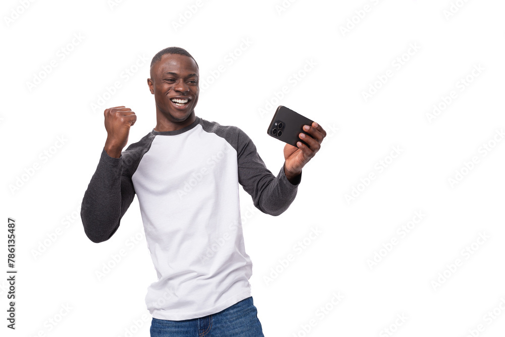 young positive african man dressed in a spring jacket feels joy holding a smartphone
