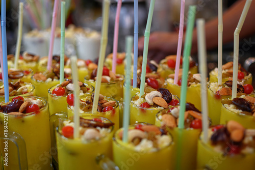 Refreshing Lassi, blended with yogurt and mango, garnished with pistachios, dates, cashews, almonds, cherries, raisins and other ingredients displayed in a food stall for sale. Selective Focus