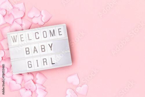 Welcome baby girl. Lightbox with letters and confetti in a heart shape on a pink pastel background.