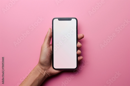 Woman's hand holding mobile phone with white empty screen in front of pink background with copy space. © Firn