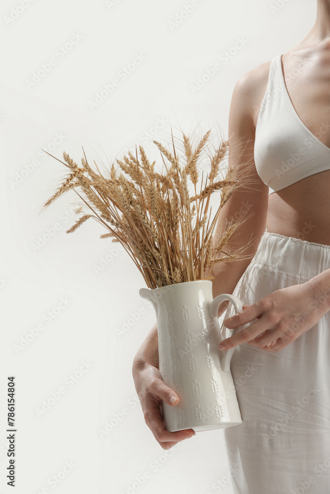 Fototapeta premium Young woman holding ceramic pitcher with wheat spikes bouquet, Celiac Disease And Gluten Intolerance
