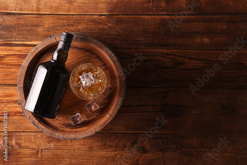 Whiskey with ice cubes in glass, bottle and barrel on wooden table, top view. Space for text