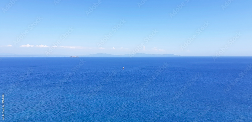 Lonely sail floats in a calm sea against a blue sky.