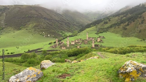 View of the medieval Targim tower complex in the Caucasus mountains surrounded by greenery. The Caucasus Mountains on a cloudy day in Ingushetia. Russia, 4K. photo