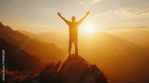 A man standing proudly atop a mountain as the sun sets, casting a warm glow over the rugged landscape