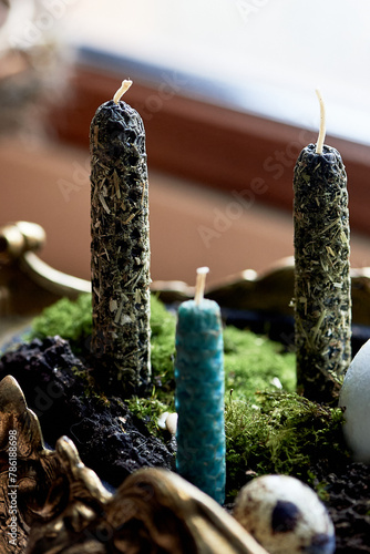 A green bowl filled with candles and moss sits on a wooden window sill, surrounded by terrestrial plants and grass. A twig and rope add to the natural houseplant landscape