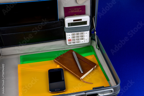 Briefcase with Notebook Pen Mobile Phone Calculator and Files on a Blue Surface